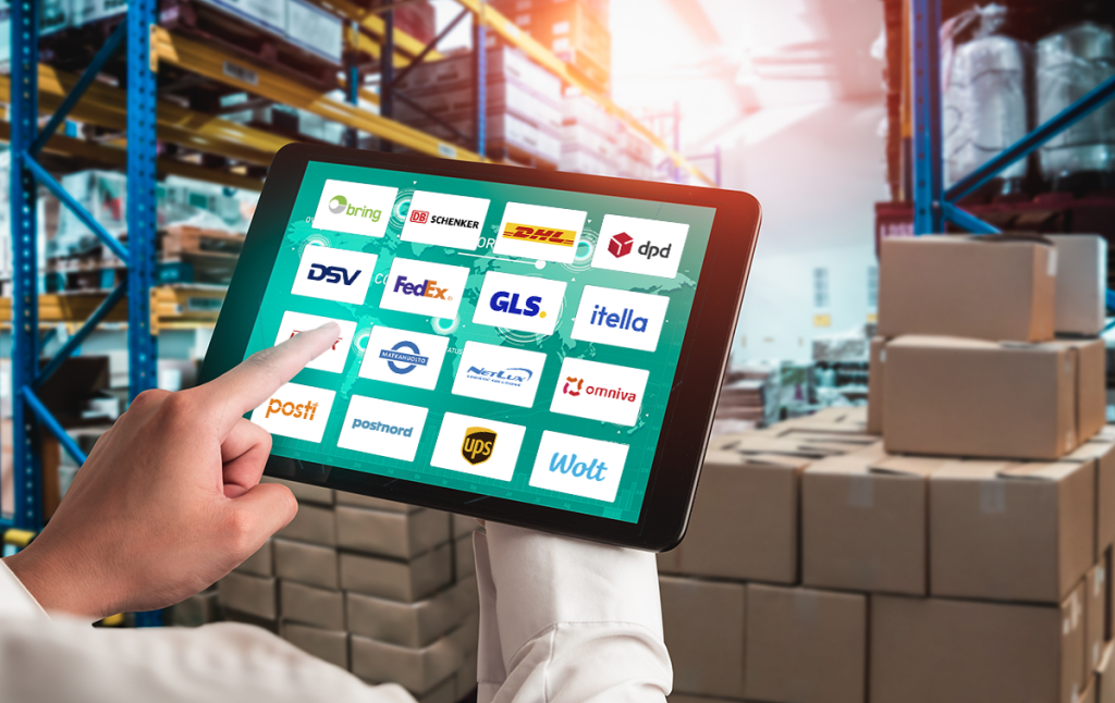 Isik kasutab laos tahvelarvutit, mille ekraanil on nähtavad mitmete kuller- ja logistikafirmade logod, näiteks Posti, DHL, GLS, UPS ja Wolt.